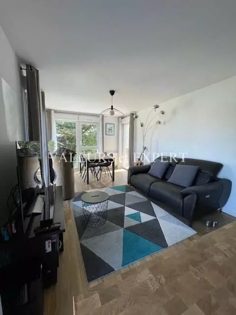 Grand séjour avec parquet clair, murs blancs et baie vitrée donnant sur l’extérieur.