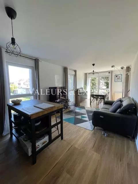 Grand séjour avec parquet clair, murs blancs et baie vitrée donnant sur l’extérieur.