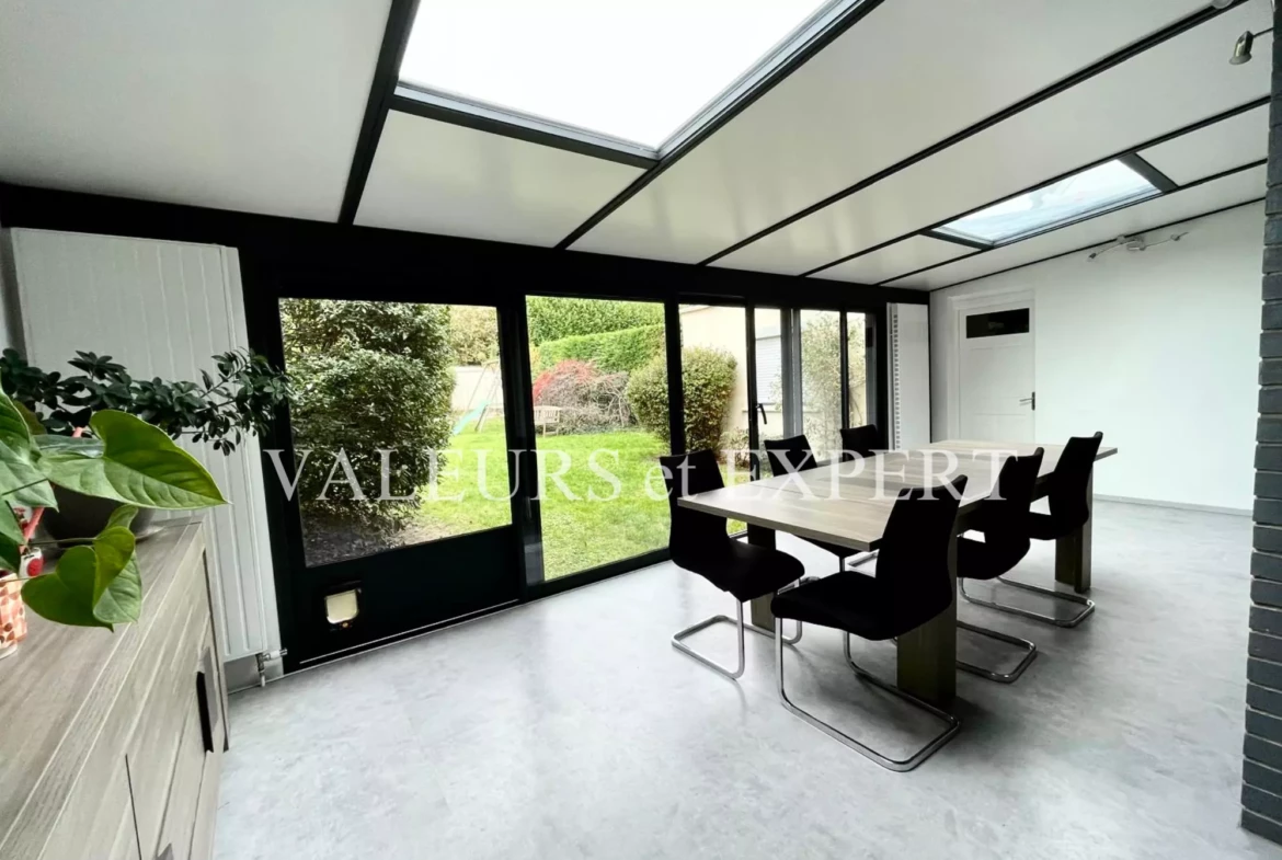 Salle à manger lumineuse avec véranda et grandes baies vitrées donnant sur le jardin.