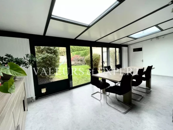 Salle à manger lumineuse avec véranda et grandes baies vitrées donnant sur le jardin.