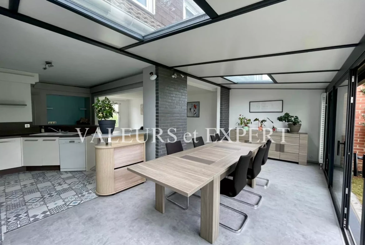 Espace repas lumineux avec grandes baies vitrées et cuisine ouverte dans une maison familiale.