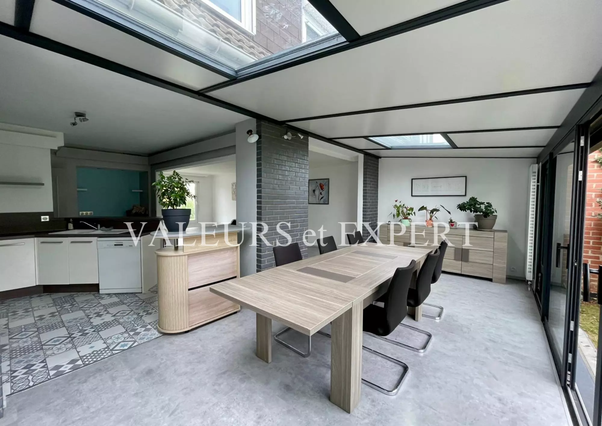 Espace repas lumineux avec grandes baies vitrées et cuisine ouverte dans une maison familiale.