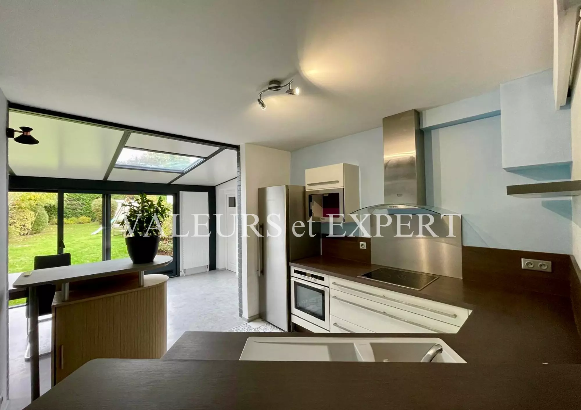 Cuisine équipée moderne avec vue sur le jardin depuis la véranda.