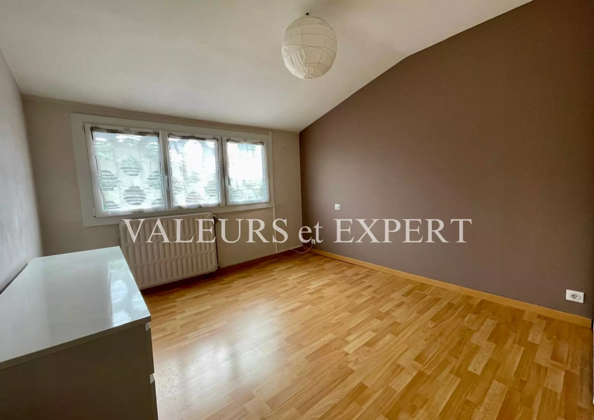 Chambre spacieuse et lumineuse avec parquet et grande fenêtre.
